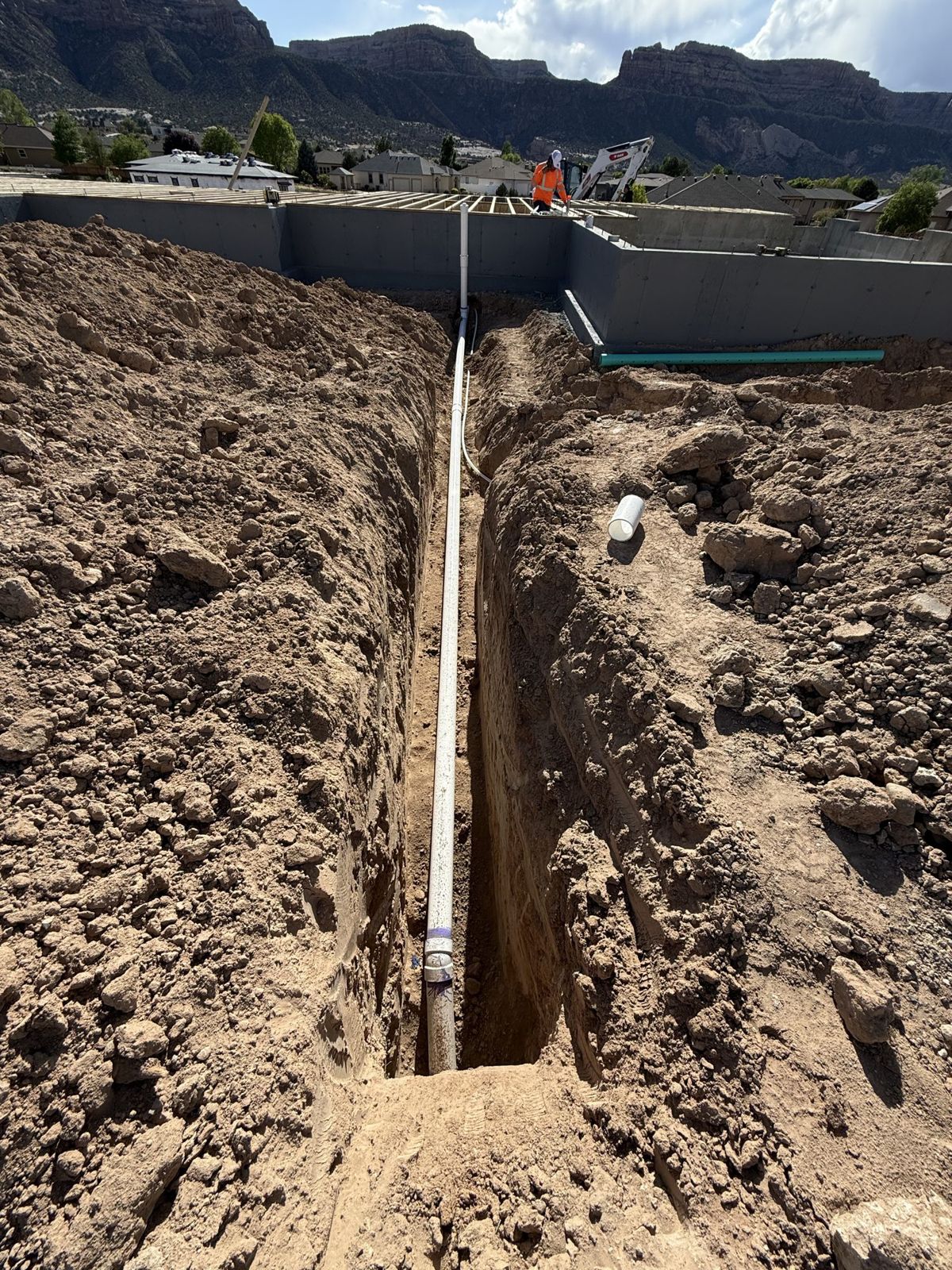 A utility trench with pipe laid beside a new foundation, red cliffs behind